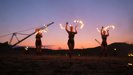 Fire-show-three-women-in-their-hands-twist-burning-spears-and-fans-in-the-sand-with-a-man-with-two-flamethrowers-in-slow-motion